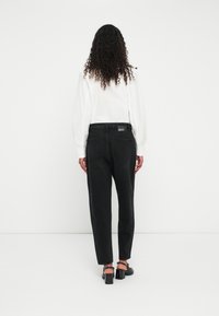 Čierne nohavice s vysokým pásom a úzkym zakončením, s piatimi vreckami a logo na zadnom vrecku. Tkanina má jemnú štruktúru, skombinované s bielou blúzkou.