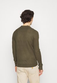 Oliwkowozielony sweter z dzianiny o teksturowanym, prążkowanym wzorze; długie rękawy, okrągły dekolt i dopasowany dół. Wykonany z miękkiego, oddychającego materiału.
