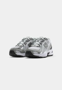 Un par de zapatillas de correr de malla blancas y grises con suelas negras, con los cordones atados, colocadas una al lado de la otra sobre un fondo blanco.
