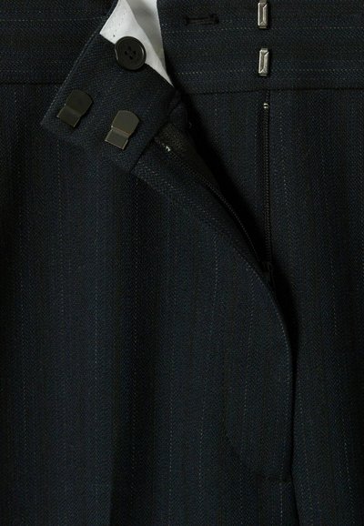 Pantaloni tailored neri scuri con righe verticali. Presentano una zip in metallo, due chiusure a gancio e una fodera in bianco a contrasto nella vita.