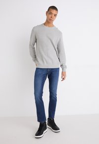 Lys grå genser med rund hals, middels tekstur, kombinert med mørkeblå rette jeans og svarte høye joggesko med hvite såler.