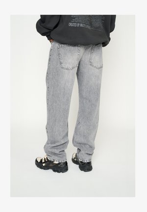 Baggy, lichtgrijze denim jeans met een vervaagd effect, voorzien van twee achterzakken en gecombineerd met zwart en beige sneakers.