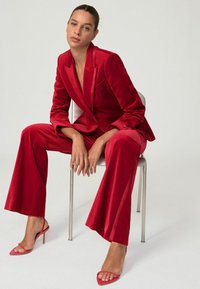 Röd sammetkostym med en skräddarsydd kavaj och vida byxor. Rosa sandaletter med klackar och remmar. Slät textur med en lyxig finish.