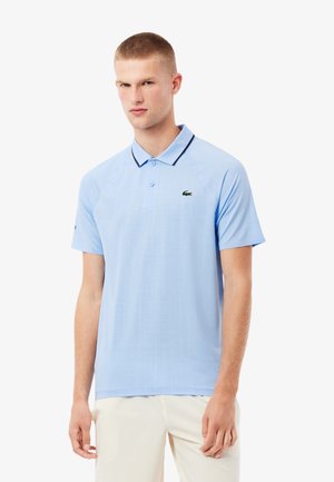 Lichtblauwe polo met een gestructureerd patroon, contrasterende donkere kraag, een twee-knopen sluiting, en een groen geborduurd logo op de borst.