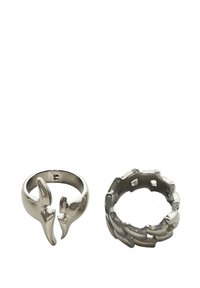 Kaksi hopeasormusta valkoisella taustalla; vasemmassa sormuksessa on avonainen claw-tyylinen muotoilu, oikeassa sormuksessa on ketjumuotoilu ympäri rengasta.