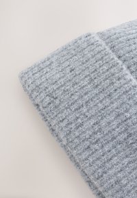 Grijze gebreide muts met een geribbelde textuur, gemaakt van zachte garen. Het ontwerp heeft een omgeslagen boord voor extra warmte en comfort.