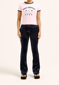 Růžové zkrácené tričko s námořnickými akcenty, na kterém je text 'JUICY COUTURE 1997 CALIFORNIA'; námořnické sametové kalhoty s elastickým pasem a zvonovými nohavicemi.