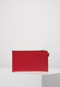 Clutch de cuero rojo texturizado con forma rectangular, cremallera dorada y diseño minimalista, con una correa para la muñeca en un lado.