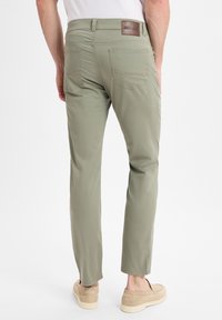 Helle grüne Hosen aus einem weichen Stoff verfügen über einen geraden Schnitt, sichtbare Gesäßtaschen und ein braunes Lederpatch am Bund.