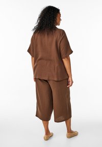 Hnedý štruktúrovaný dvojdielny outfit pozostávajúci z voľného trička s krátkymi rukávmi a širokými skrátenými nohavicami, doplnený o svetlú obuv.