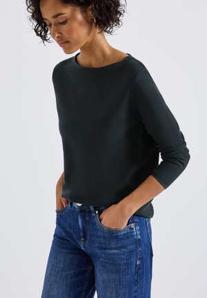 Un pull en tricot vert foncé avec un col rond et des manches trois-quarts, associé à un jean en denim bleu. Design simple et ajusté.