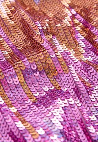 Tissu en sequins fuchsia et or rose avec des sequins circulaires disposés en rangées ondulées, créant une surface texturée et réfléchissante.