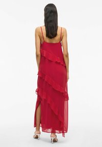 Raudona šifono suknelė su sluoksniuotais volanais, spaghetti tipo petnešėlėmis ir aukštomis šoninėmis plyšiais, pasižyminti laisvu siluetu ir lengvu tekstūru.