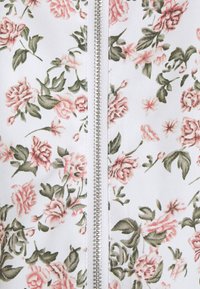 Blommig zip-up jacka i vitt med rosa rosor och gröna blad. Har en silverfärgad dragkedja i mitten för stängning. Slät textur.