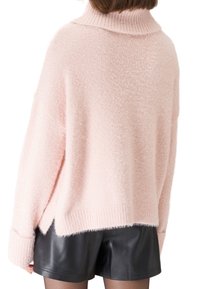 Helles rosa, flauschiges Sweatshirt mit hohem Kragen, übergroßer Passform, gerippten Bündchen und seitlichen Schlitzen, getragen über schwarzen Leder-Shorts.
