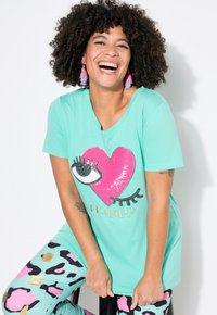 Turkis t-shirt med et pink hjerte og øje-grafik, guld "Happy" tekst, parret med leggings i sort og pastellpink leopardprint.