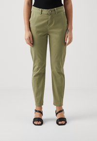 Kakhifärgade avsmalnande byxor gjorda av mjukt tyg, med sidofickor, bältesöglor och en enkel knappstängning. Svarta remsandaler.