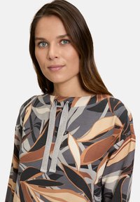 Patterned long-sleeve top featuring a multicolored leaf design in earthy tones with a ribbed texture and gray drawstrings at the neck.