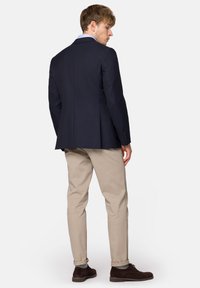 Granatowa marynarka, dopasowany fason, z dwoma wentylacjami z tyłu, zestawiona z jasnobeżowymi chinosami i brązowymi butami. Subtelna tekstura na tkaninach.