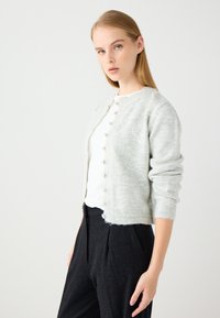 Hellgrauer, gestrickter Cardigan mit rundem Halsausschnitt, Knopfverschluss vorne, gerippten Bündchen und Saum. Kombiniert mit dunklen, taillierten Hosen.