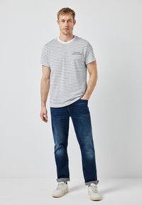 Pruhované tričko s krátkým rukávem v bílé a námořnické modré barvě s kulatým výstřihem, spárované s tmavě modrými džíny a bílými teniskami. Uvolněný střih, ohrnuté manžety.