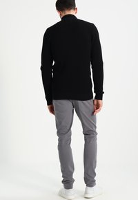 Schwarzer Strickpullover mit strukturiertem Design, kombiniert mit hellgrauen Slim-Fit-Hosen und weißen Turnschuhen. Die Sicht ist von hinten.