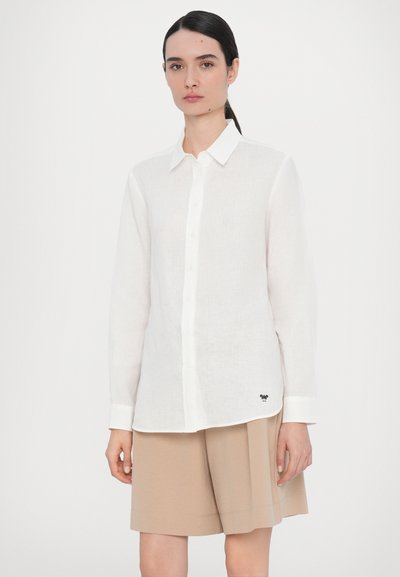 White linen button-up shirt with long sleeves, featuring a classic collar and a small black embroidered logo at the hem.