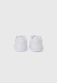 Baskets en cuir blanc avec une texture lisse, dos arrondi et semelle en caoutchouc plate. Présente un design épuré et un branding subtil sur le talon.