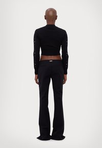 Sweater preto cropped com mangas longas, apresentando taxas decorativas. Combinado com calças flare pretas de cintura alta com bolsos.