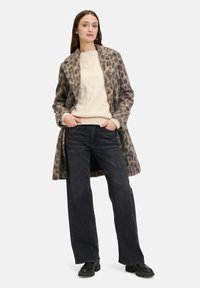 Tiermuster-Mantel in Grau und Braun, kombiniert mit einem cremefarbenen Pullover und schwarzen, weit geschnittenen Jeans. Strukturierter Stoff und lässige Silhouette. Schwarze Stiefel.