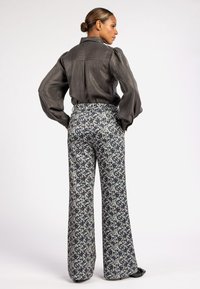 Grijze, getextureerde blouse met opschopmouwen, gecombineerd met hoge, wijde broek met een blauw bloemenpatroon op een lichte achtergrond.