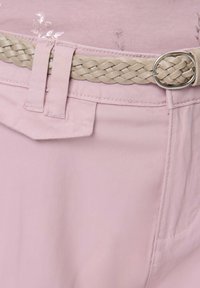 Jasnoróżowe spodnie z plecionym beżowym paskiem. Posiadają kieszenie i subtelne kwiatowe wzory na tkaninie, tworząc delikatną teksturę.