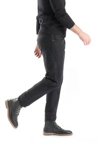 Pantalons en denim noir associés à des bottes en cuir noir à lacets. La tenue présente une coupe slim et une texture lisse tout au long.