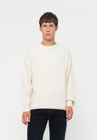 Crème ribgebreide trui met een ronde halslijn en verlaagde schouders, gecombineerd met donkere jeans. Zachte textuur en een relaxed pasvorm.