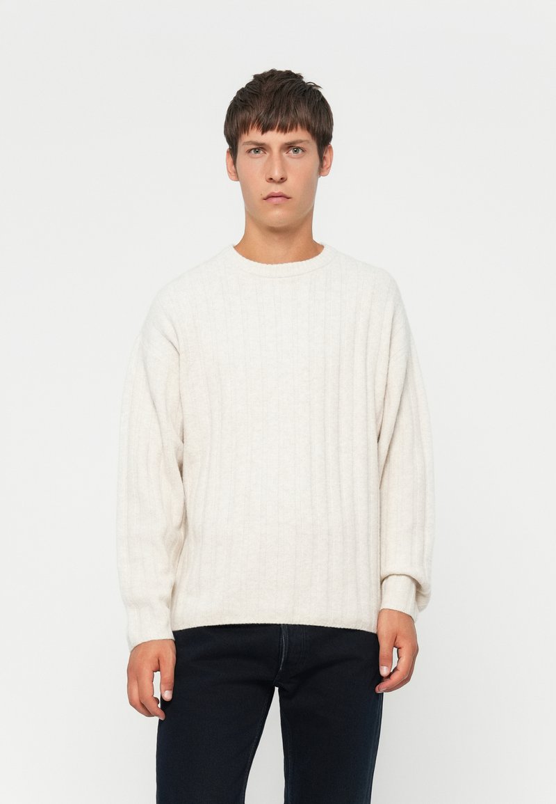 Crème ribgebreide trui met een ronde halslijn en verlaagde schouders, gecombineerd met donkere jeans. Zachte textuur en een relaxed pasvorm.