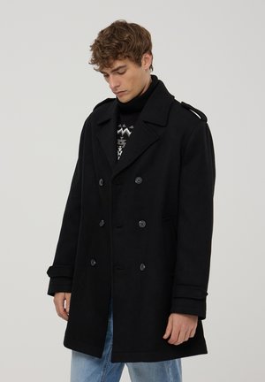 Cappotto in lana nera con design doppiopetto, ampi revers e due tasche frontali. Dotato di un colletto alto e dettagli con bottoni.