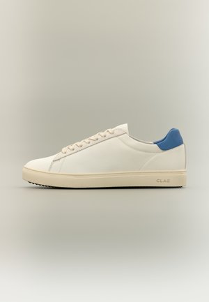 Hvid lav sneakers med flødefarvet sål og blå hælkappe, med snørelukning og mærket "CLAE" på siden af sålen.