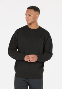 Svart crewneck sweatshirt gjord av mjukt material, med ribbad halsringning och ärmar, samt en diskret logotypdetalj på bröstet.