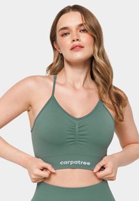 Svetlo zelena športna modrček z v-izrezom, nabrano sprednjo zasnovo, tankimi naramnicami in blagovno znamko na dnu sloganom "carpatree".