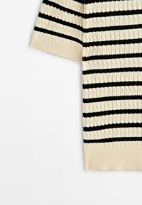 Pull tricoté à manches courtes en crème et noir, présentant un motif texturé et des rayures horizontales. Bordures côtelées aux extrémités.