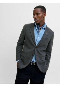 Kolkgrå kavaj i strukturerad tyg, med två framfickor och enkel knäppning, bärs över en denimskjorta med en bandana.