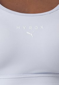 Svetlo lavender športna majica brez rokavov, izdelana iz gladkega blaga, z embosiranim napisom "HYROX" in logotipom Puma v beli barvi na prednjem delu.