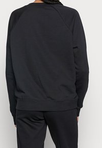 Svart sweatshirt med raglanärmar, ribbad manschetter och nederkant, mjukt tyg, minimalistisk design, inga synliga logotyper eller mönster.