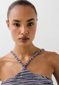 Un primo piano di un top realizzato in un tessuto multicolore e strutturato, con una scollatura a halter e un dettaglio di tracolla attorcigliata.