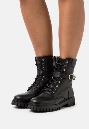 Sorte ankelstøvler i læder med snørelukning foran, lynlås, tykke gummisåler, guldfarvede snørehuller og en rem med spænde.