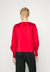 Punane satiinist pluus puff-sleeved käistega, volangkaelusega ja kitsaste mansettidega. Üksnes seljaosa, sile tekstuur, kombineeritud mustade pükstega.