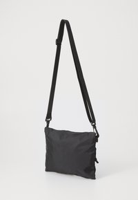 Zwarte schoudertas gemaakt van lichtgewicht nylon. Heeft een slank rechthoekig ontwerp met een verstelbare riem en een getextureerd oppervlak.