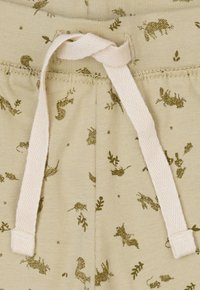 Pantalons de survêtement beige clair avec une texture douce, un waistband élastique, un cordon de serrage blanc contrastant et de petits motifs d'animaux et de plantes verts foncés.