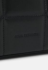 Borsa a tracolla in pelle nera con un design trapuntato, caratterizzata da cuciture visibili e un logo impresso "JULIA SKERGETH" in basso.