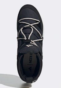 Černá sportovní bota se syntetickým svrškem, elastickými tkaničkami, polstrovaným límcem a bílou podrážkou. Uvnitř je vytištěn nápis "Moon Boost". Texturovaná podrážka pro lepší přilnavost.